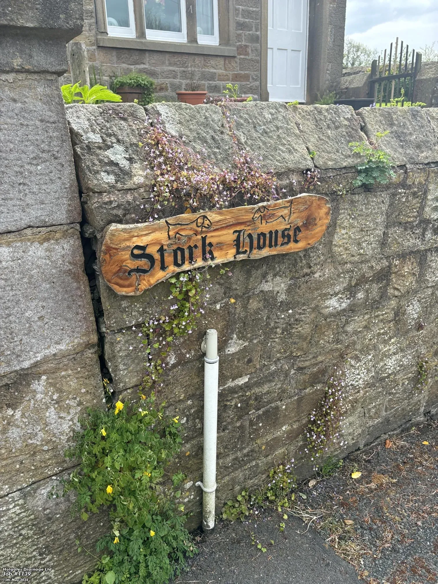 Wooden 'Stork House' property sign on a stone wall with an external pipe